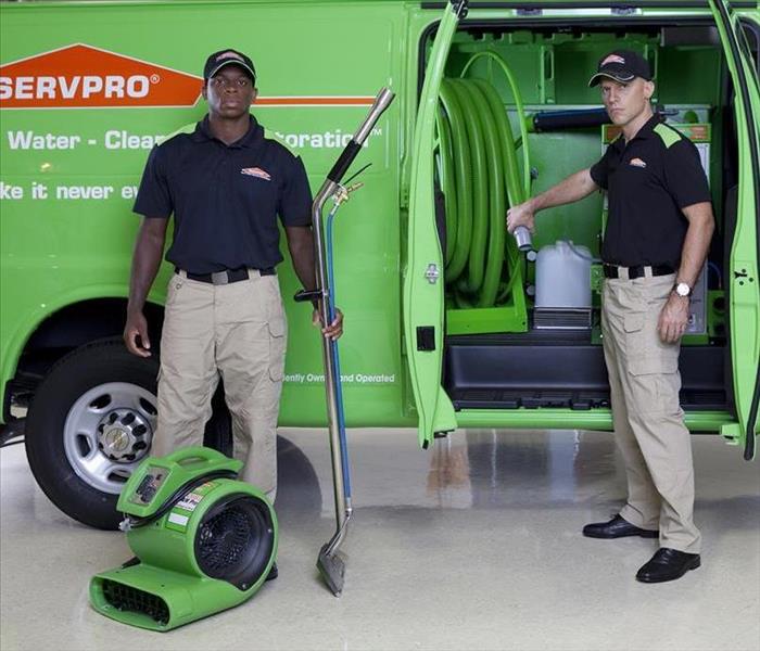 Two men in front of SERVPRO vehicle with water cleanup equipment. 
